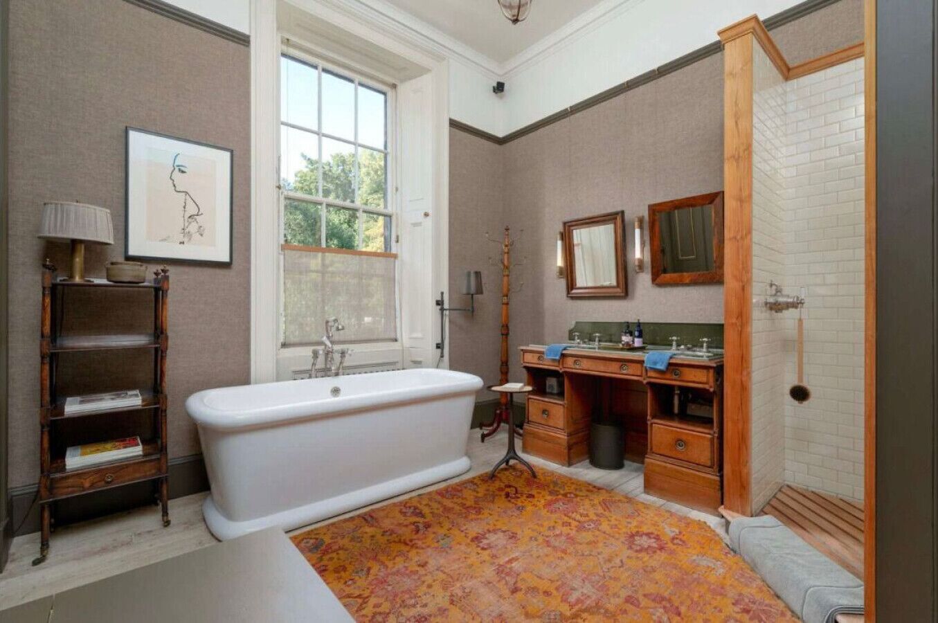 A bathroom with a freestanding bathtub, a vanity with a mirror, and a window with a view of greenery.