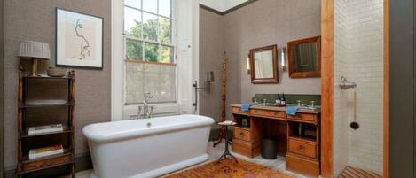 A bathroom with a freestanding bathtub, a vanity with a mirror, and a window with a view of greenery.