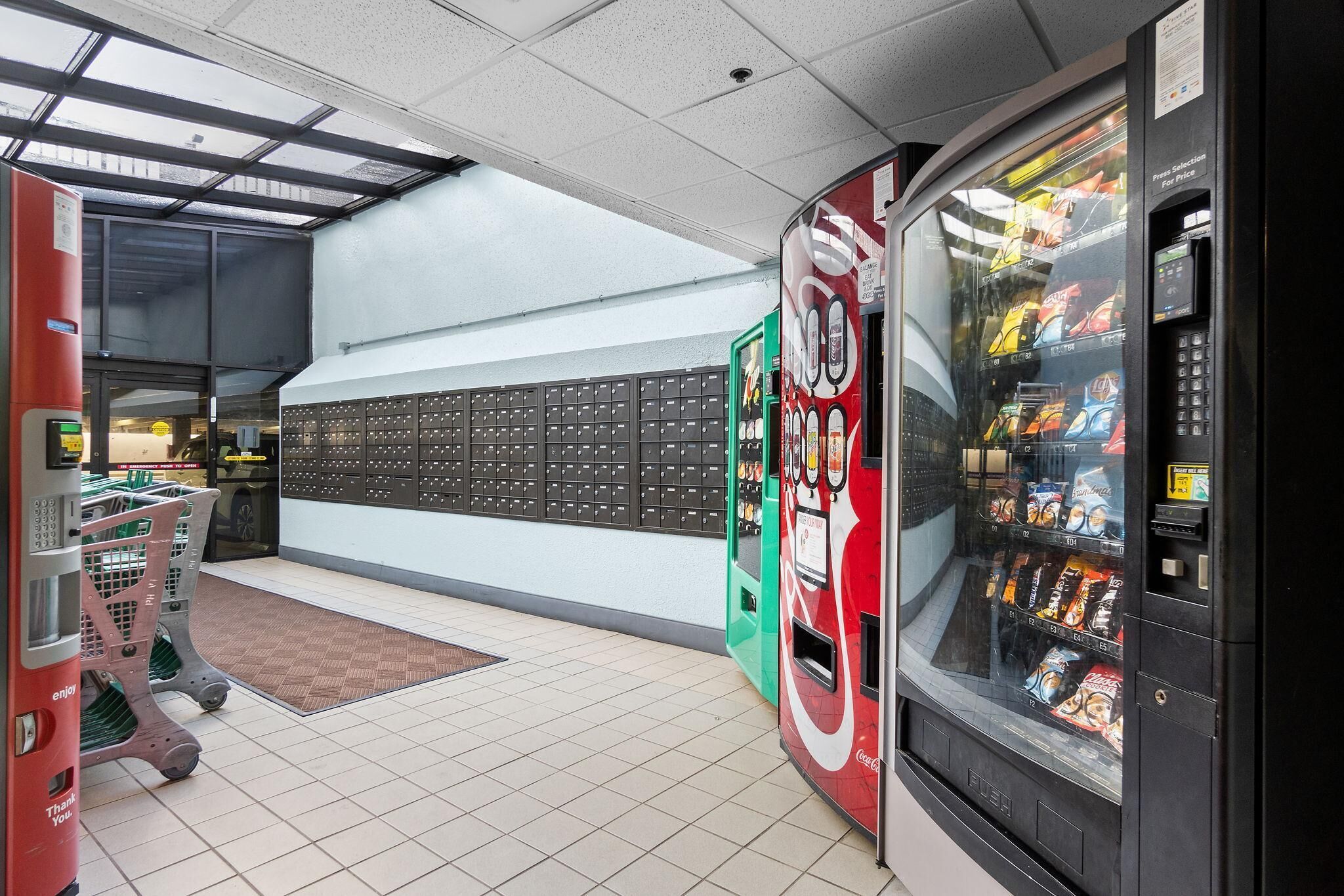 A vending machine area with a Coca-Cola branded machine, a red and green machine, and a wall with a storage unit.