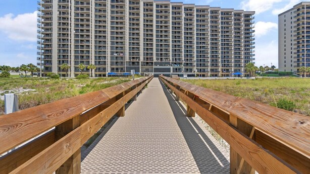 A long wooden boardwalk leading to a high-rise residential building with multiple balconies. - Phoenix 6 011 (Orange Beach)