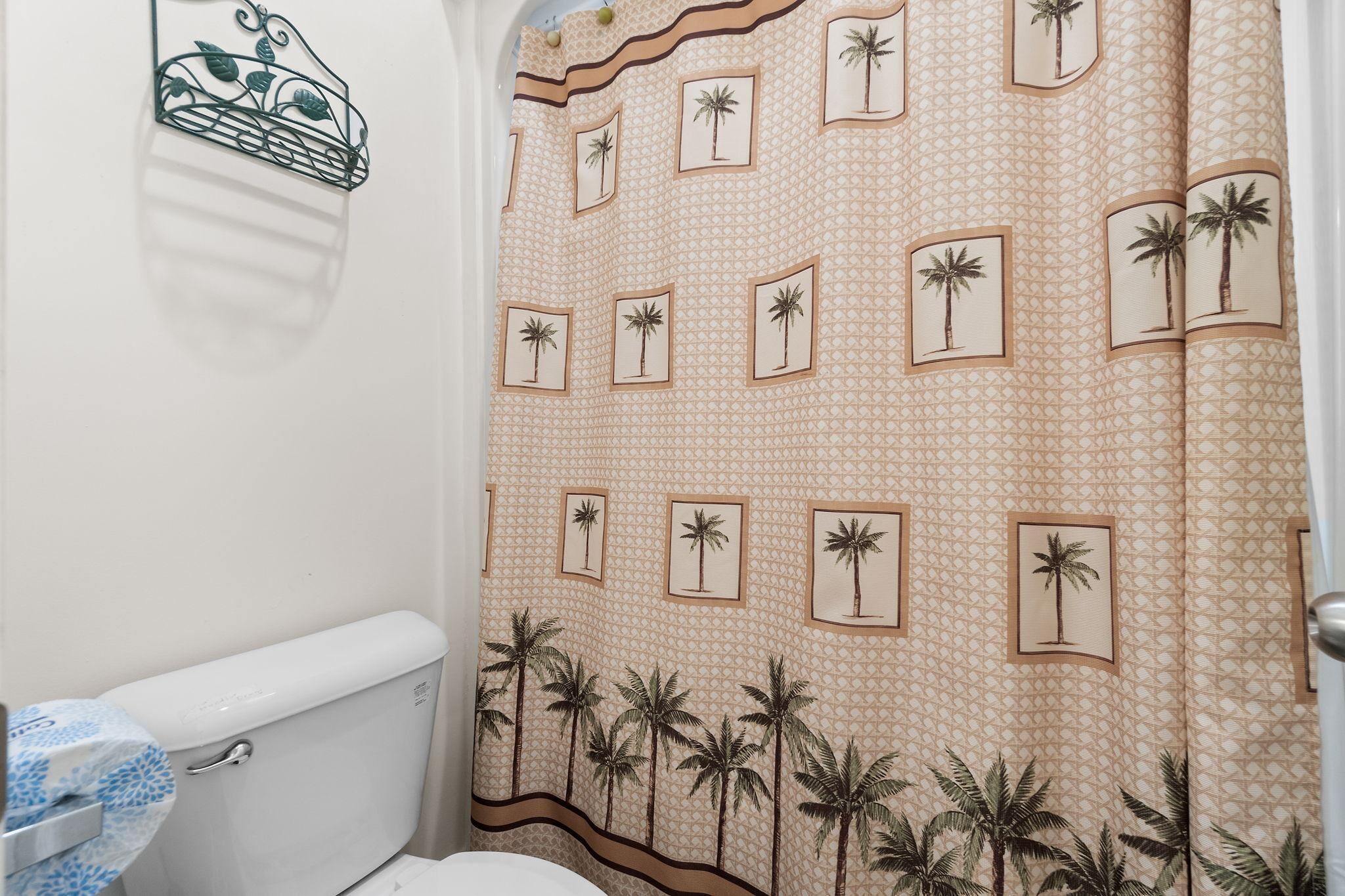 Un bagno con il water, un portasciugamani e una tenda da doccia con motivi di palme.