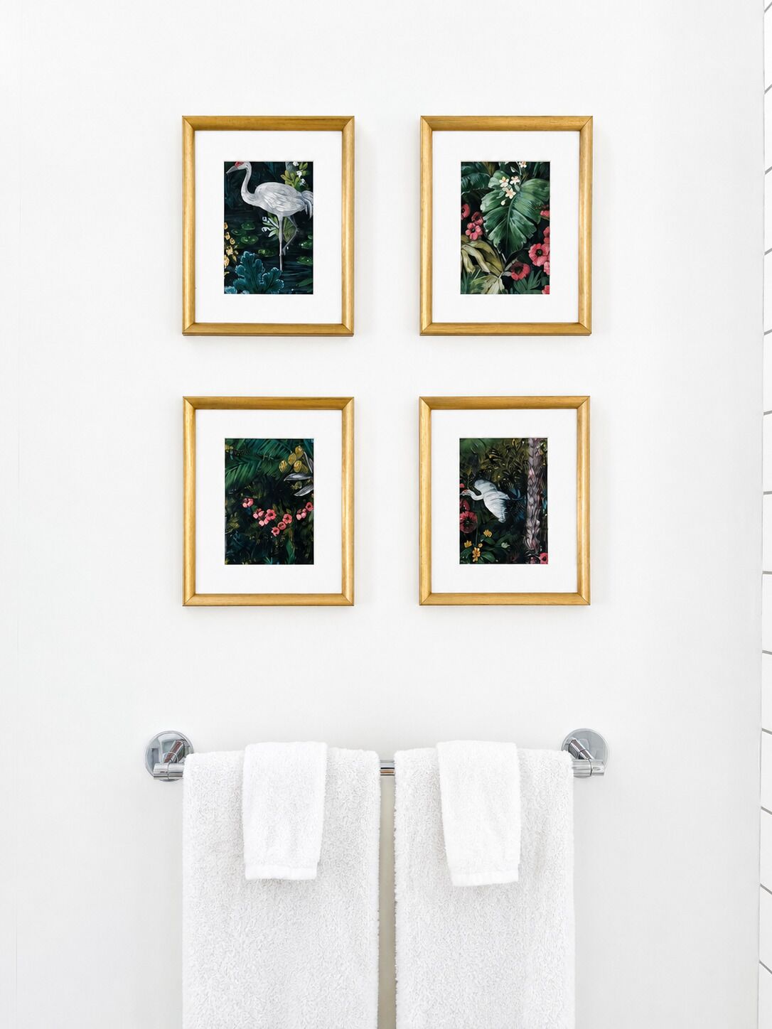 Vier gerahmte Bilder an einer Wand, zwei Handtücher hängen an einem Ablagegestell darunter.