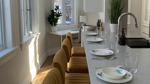 A modern kitchen with a long dining table, chairs, and a sink. - Appartements Saint-Alexandre (Longueuil)