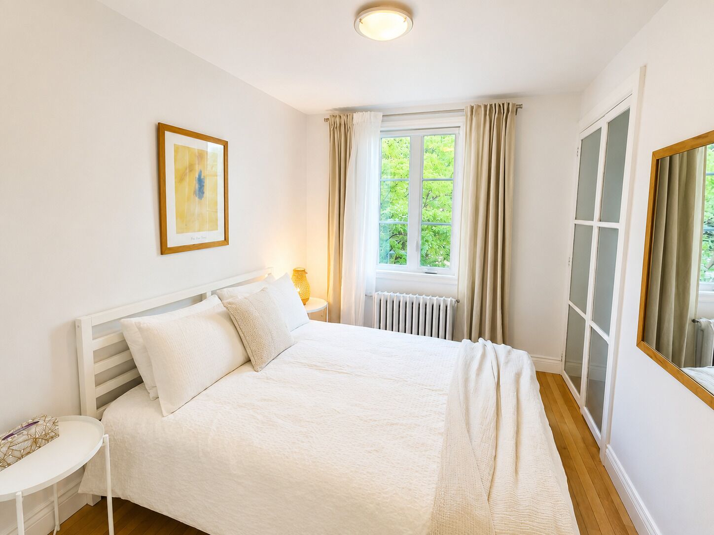 Un dormitorio con cama, mesita de noche, ventana con cortinas y radiador.
