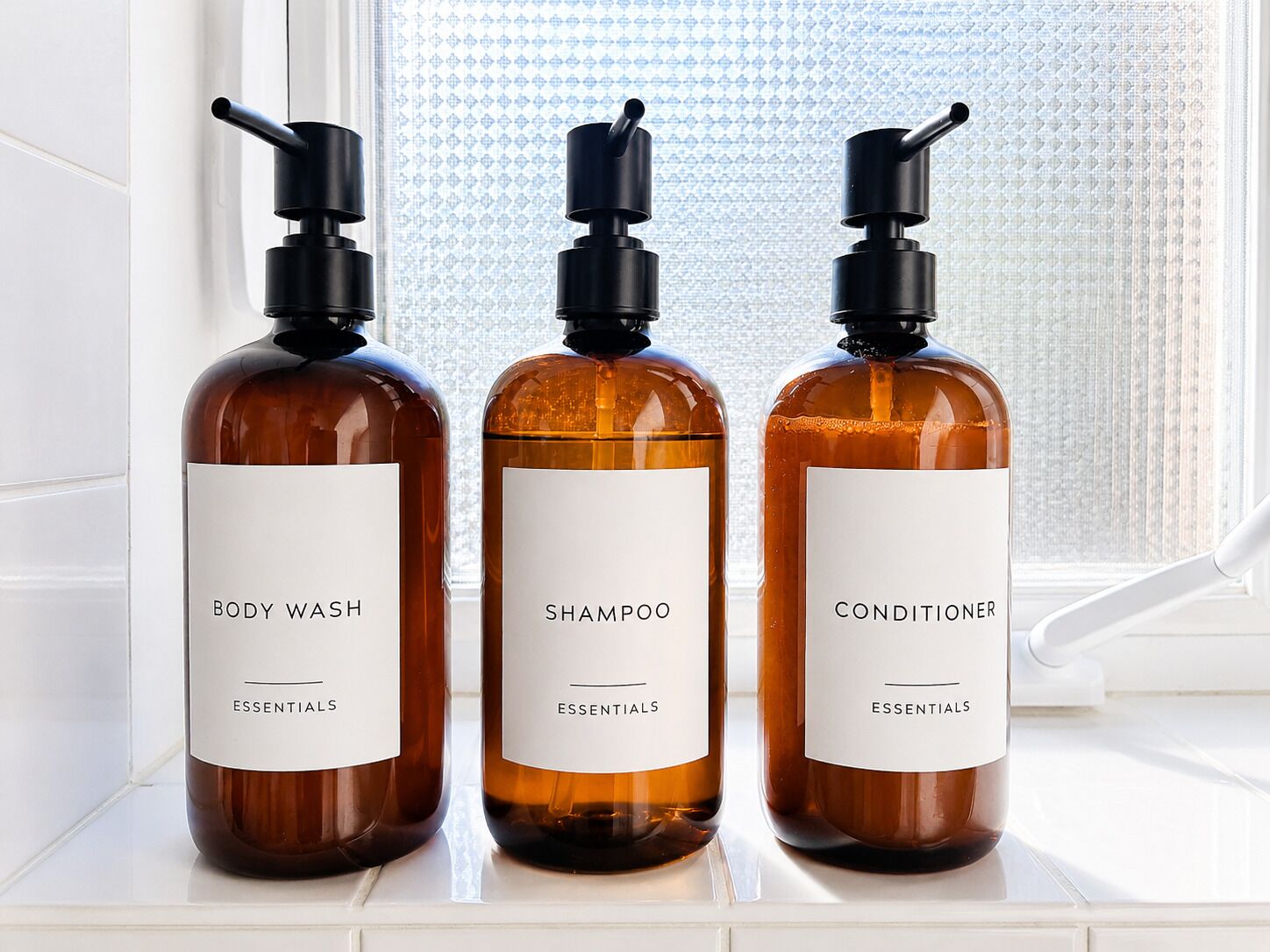 Three bottles of body wash, shampoo, and conditioner on a windowsill.