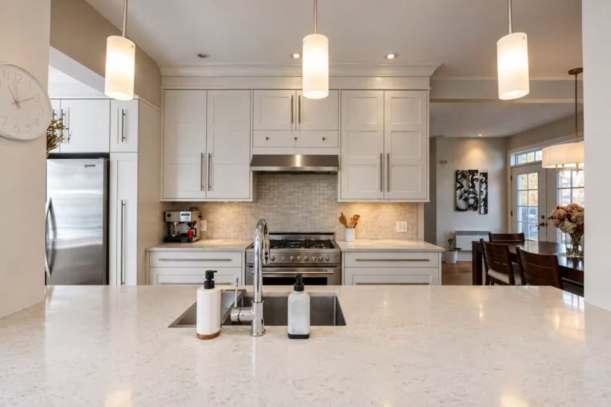 Cocina moderna con armarios blancos, electrodomésticos de acero inoxidable e iluminación colgante.