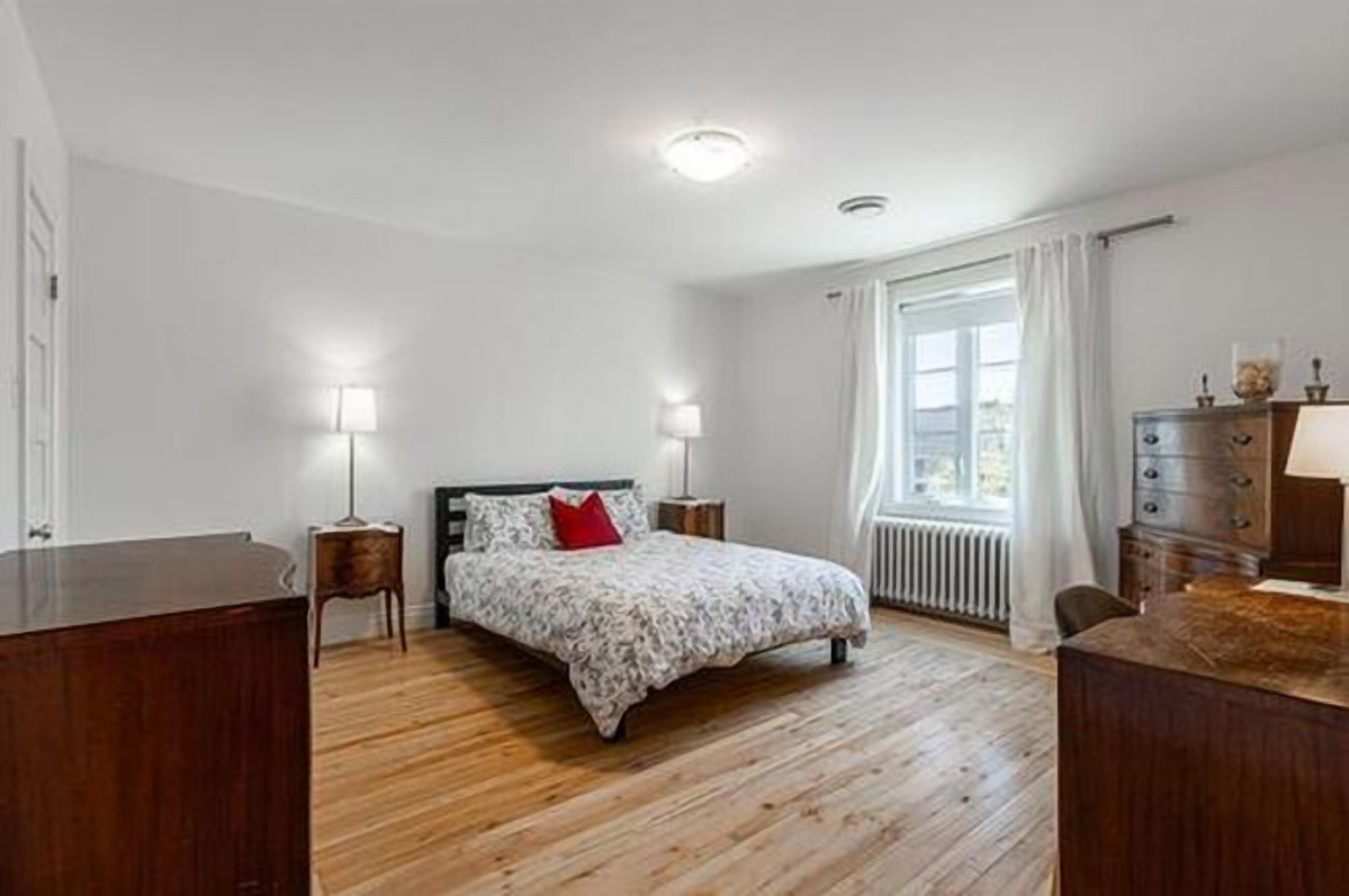 A bedroom with a bed, bedside lamps, a dresser, and a radiator.