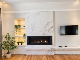 Una sala de estar moderna con chimenea, televisor montado y piso de madera.