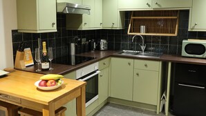 Una cocina con gabinetes verdes, una mesa de madera con fruta, un lavaplatos, una estufa y un microondas.
