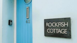 Una puerta azul con una placa que indica el número '42' y un letrero que dice 'ROCKFISH COTTAGE'.