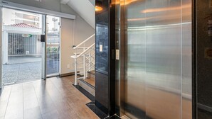 Een lift met een metalen afwerking, een trap met witte leuningen en een bordje met de aanduiding van de uitgang.
