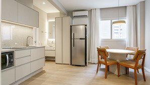 Een moderne keuken met een ingebouwde oven, een koelkast en een eethoek met een ronde tafel en stoelen.
