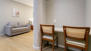 A room with a grey sofa, two wooden chairs, a white desk, and a wooden floor. - Walkable | Near Beiramar Mall #TM103 (Florianópolis)