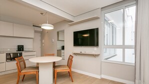 Eine moderne Küche mit Einbaugeräten, ein Essbereich mit rundem Tisch und zwei Stühlen sowie ein großer Fernseher an der Wand.