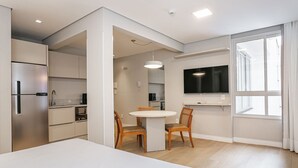 Eine moderne Küche mit Einbaukühlschrank, eine Essecke mit rundem Tisch und Stühlen, ein flachbildfernseher an der Wand und ein großes Fenster mit Vorhängen.
