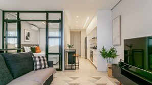 Ein modernes Wohnzimmer mit einer Couch, einem Fernseher und einer Küche im Hintergrund.
