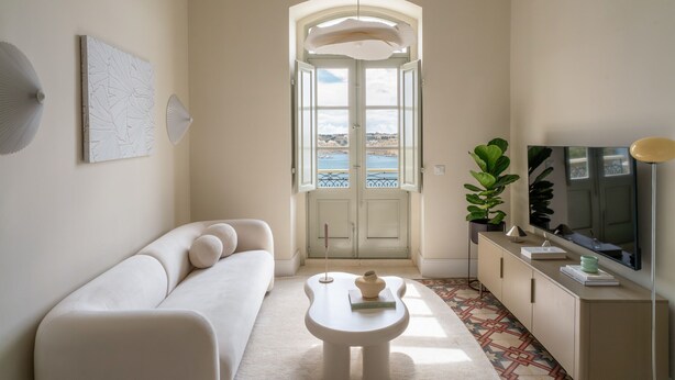 Ett modernt vardagsrum med en soffa, ett soffbord, en tv och utsikt över havet genom en dörr.