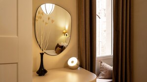 Ett litet bord som står vid sängen, med en vas, en lampa och en spegel.