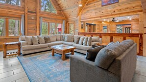 A spacious living room with a large sectional sofa, a wooden coffee table, and a blue patterned rug. - Large Hot Tub | Pool Table | Playset | Sleeps 22 (Broken Bow)