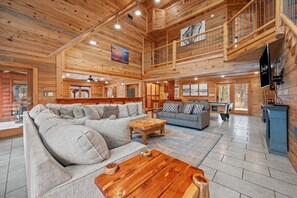 A spacious wooden interior with a large sectional sofa, a smaller sofa, and a coffee table. - Large Hot Tub | Pool Table | Playset | Sleeps 22 (Broken Bow)