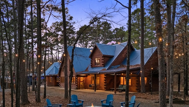 A log cabin with a fire pit and blue Adirondack chairs in a forest setting. - Large Hot Tub | Pool Table | Playset | Sleeps 22 (Broken Bow)