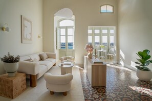 Un salon comprenant un canapé, un fauteuil, une table basse et une vue dégagée sur l’extérieur grâce à une grande fenêtre.
