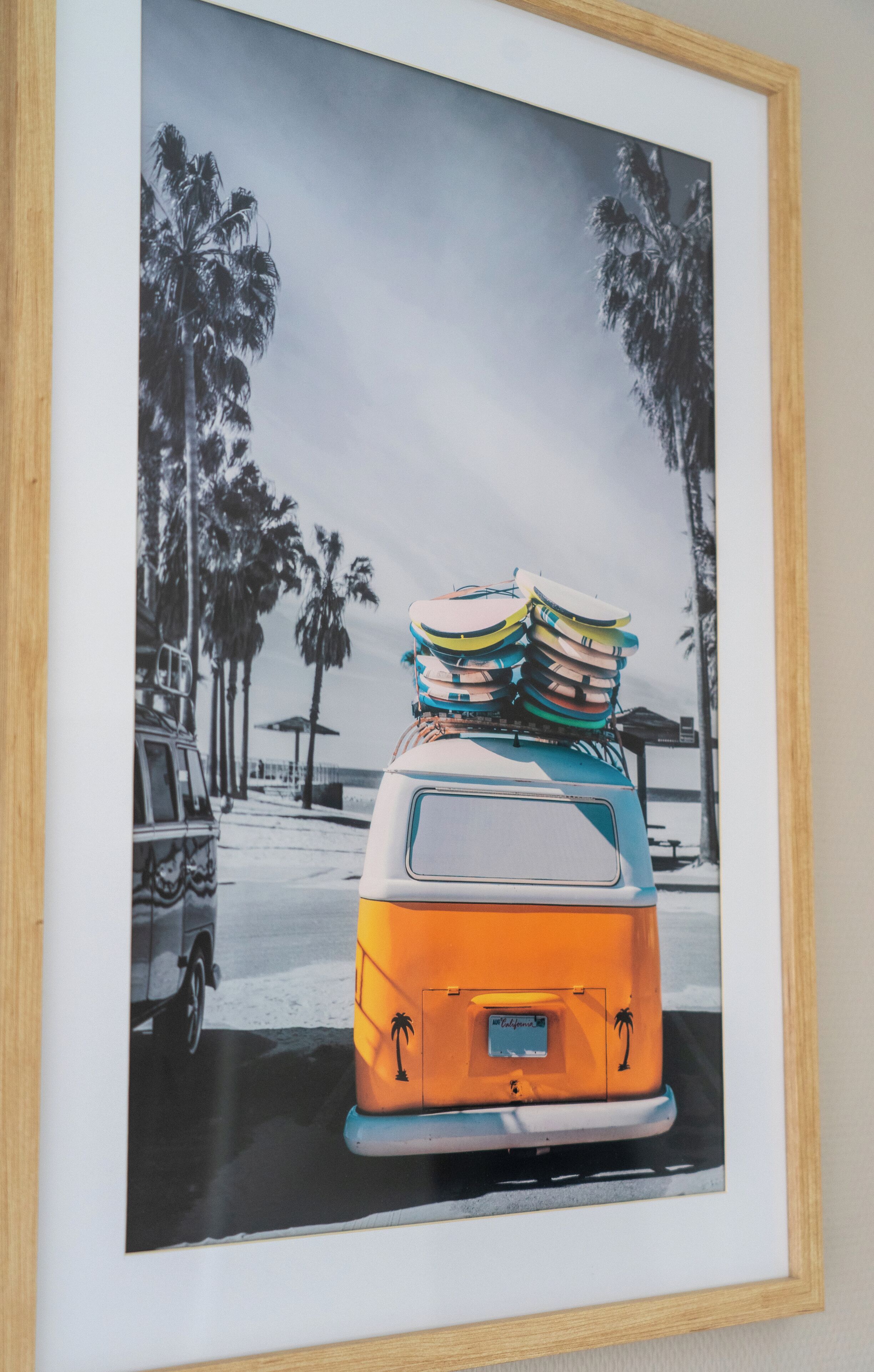 A vintage van with surfboards on the roof parked on a street with palm trees.