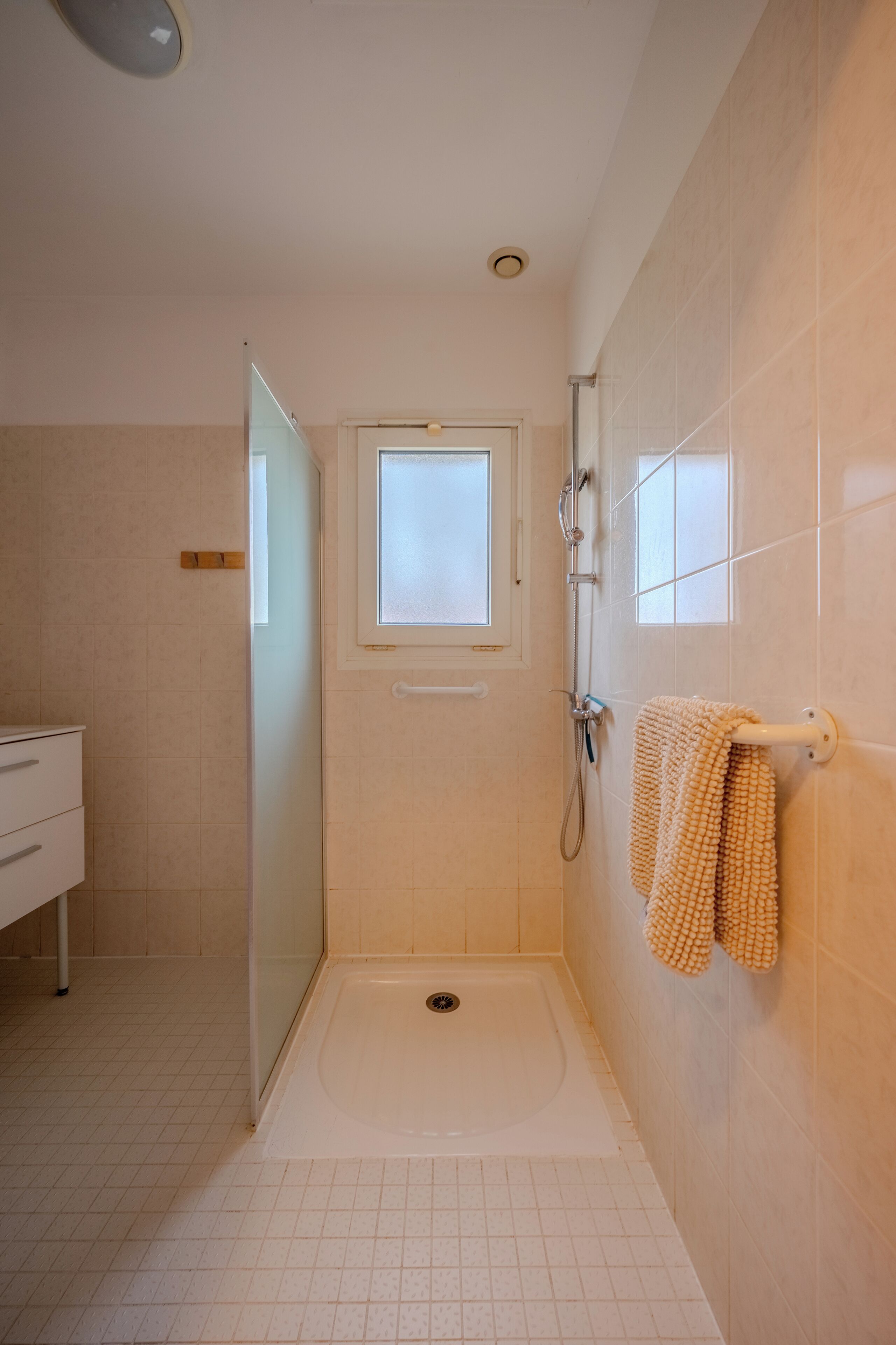 Eine ebenerdige Dusche mit Fenster, ein Handtuchhalter mit Handtuch und ein weißes Waschbecken.