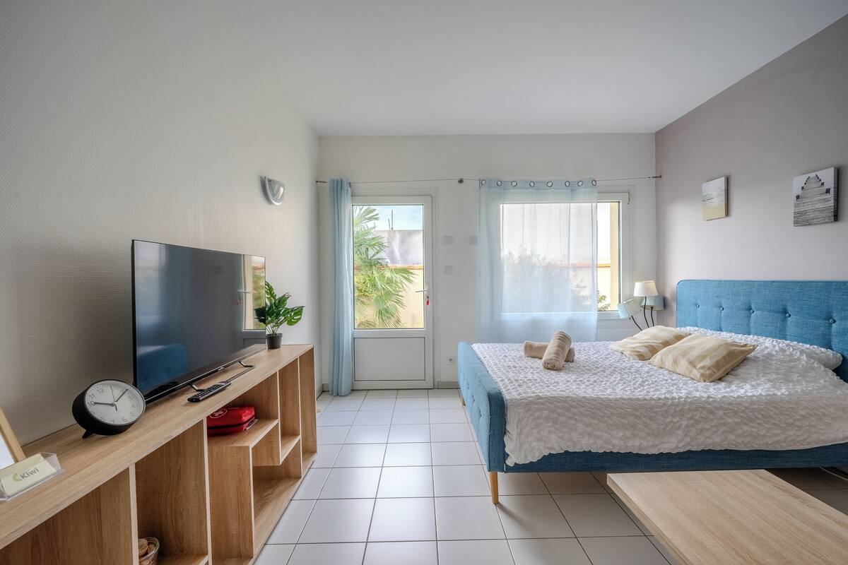 A bedroom with a bed, a TV, a clock, and a window with curtains.