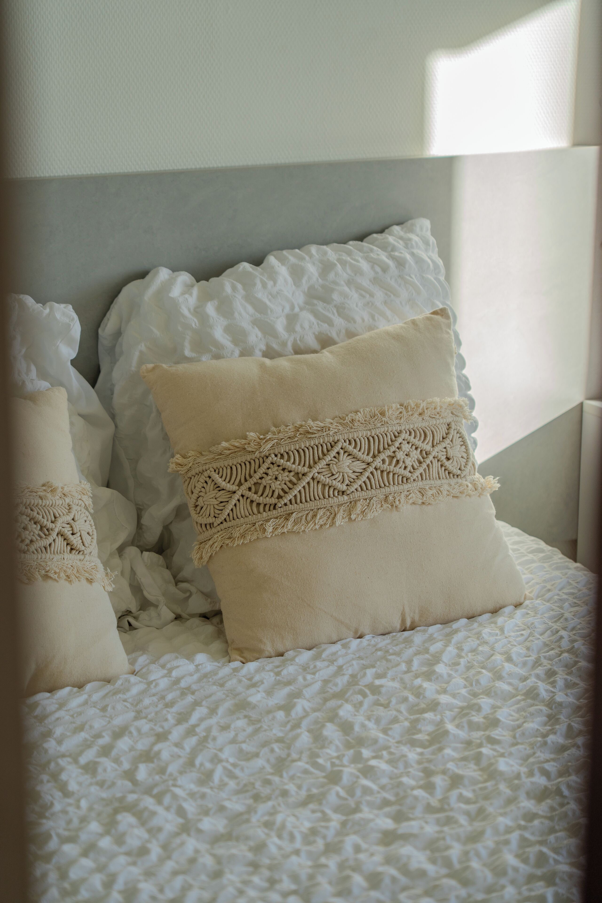 Un lit recouvert d’une couverture blanche texturée et agrémenté d’oreillers décoratifs aux motifs complexes.