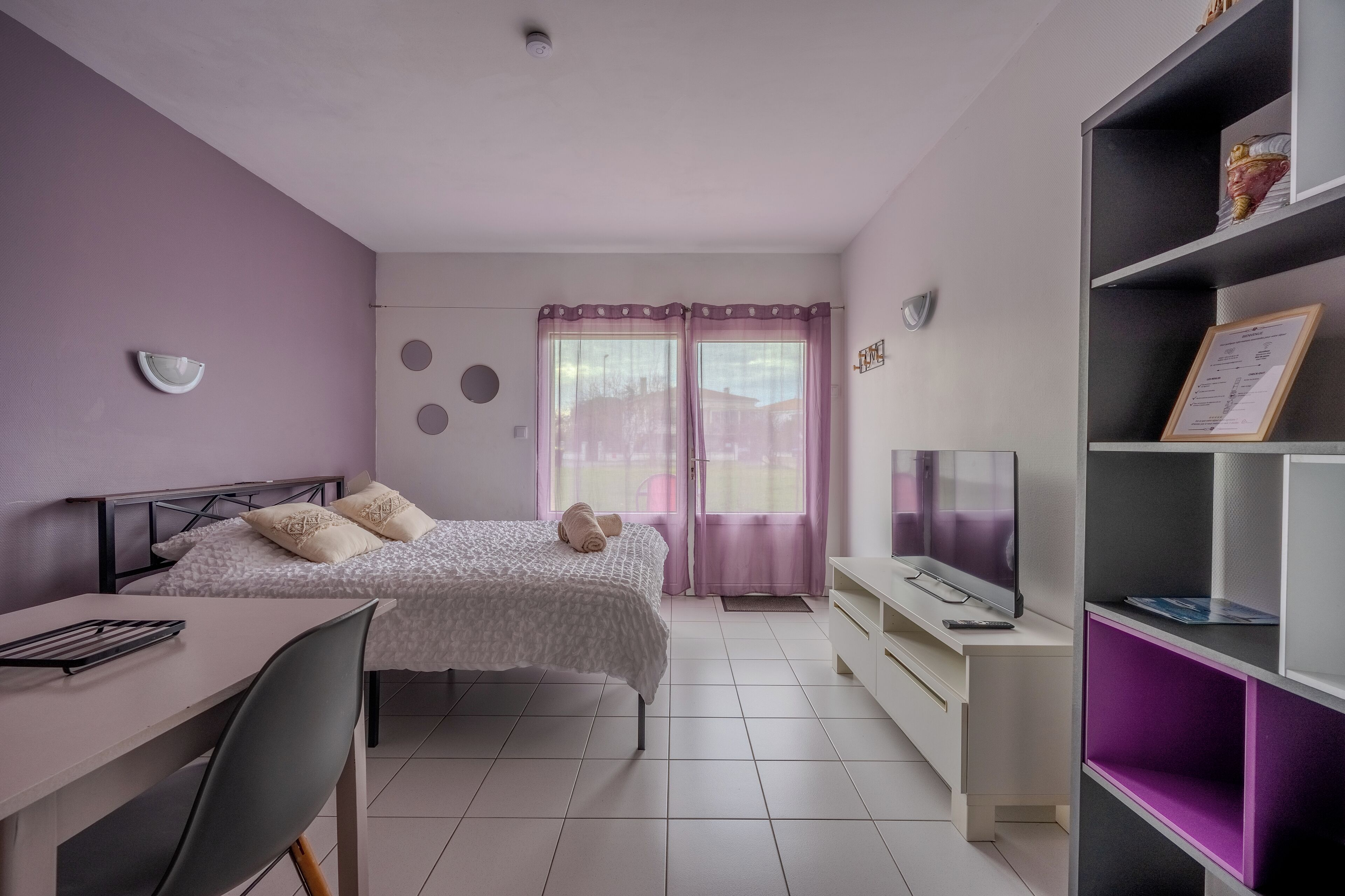 A bedroom with a bed, a desk, a TV, and a bookshelf.