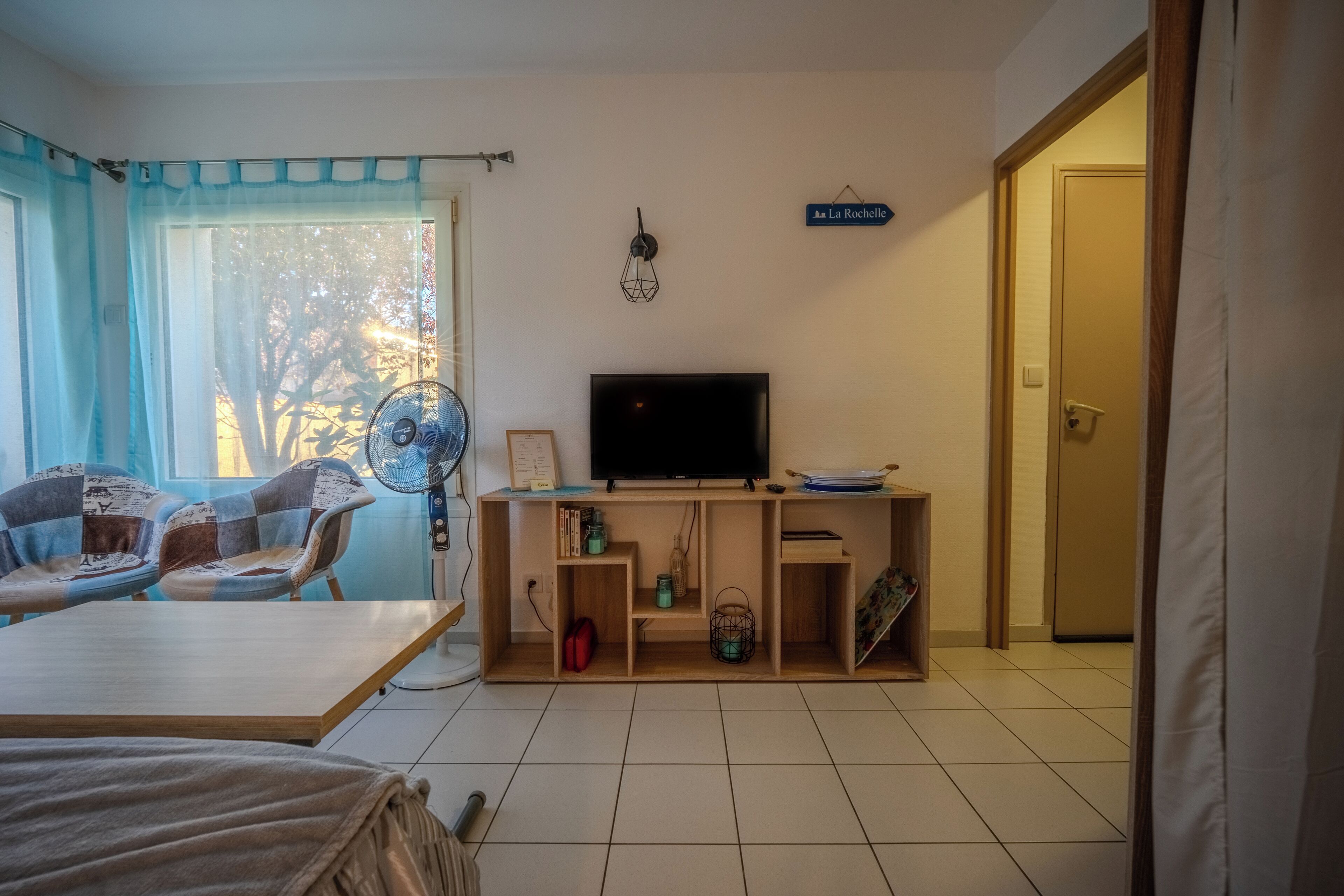 A room with a bed, a desk, a chair, a TV, and a window with curtains.