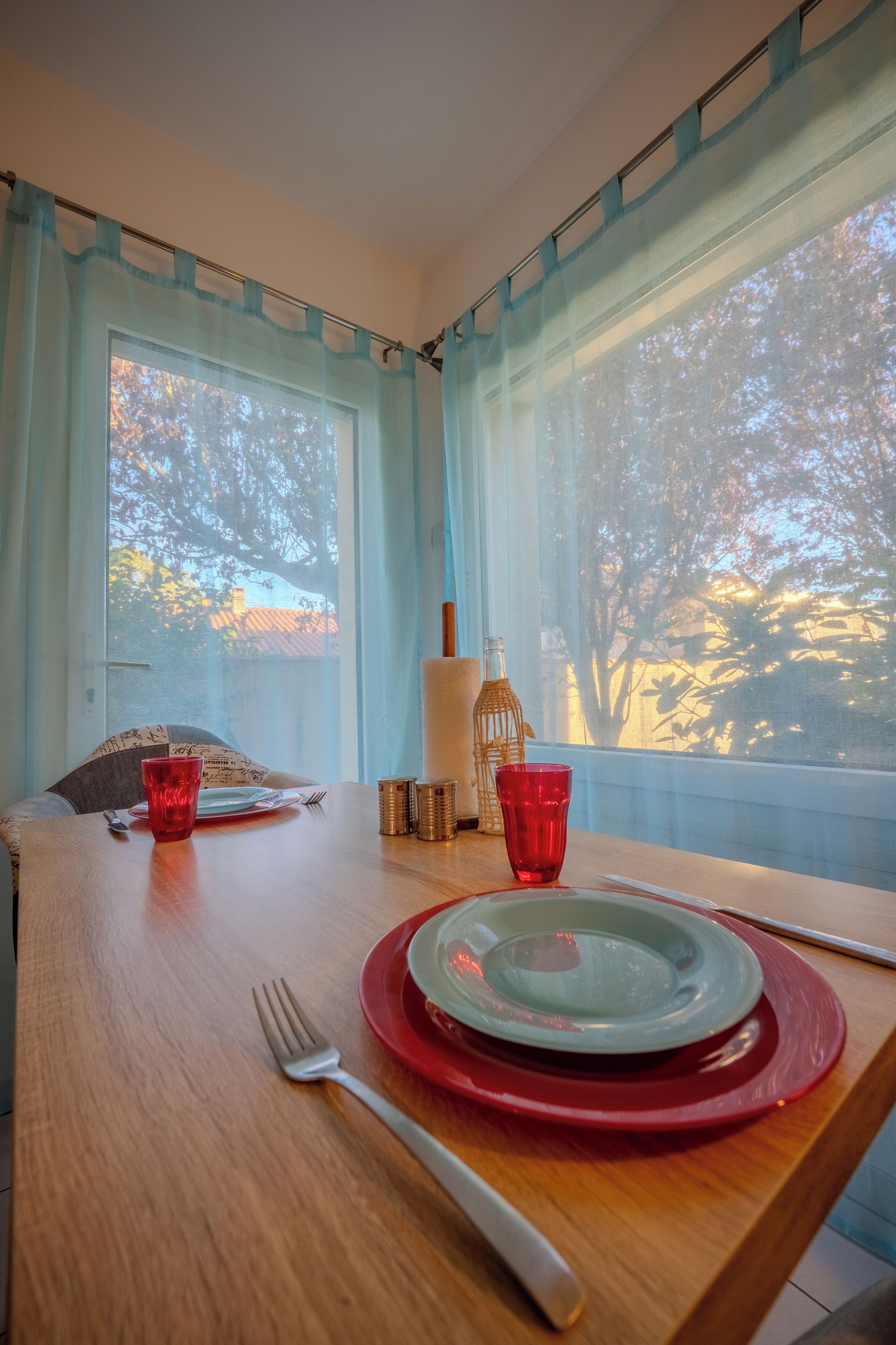 A dining table with plates, cutlery, and a red glass.