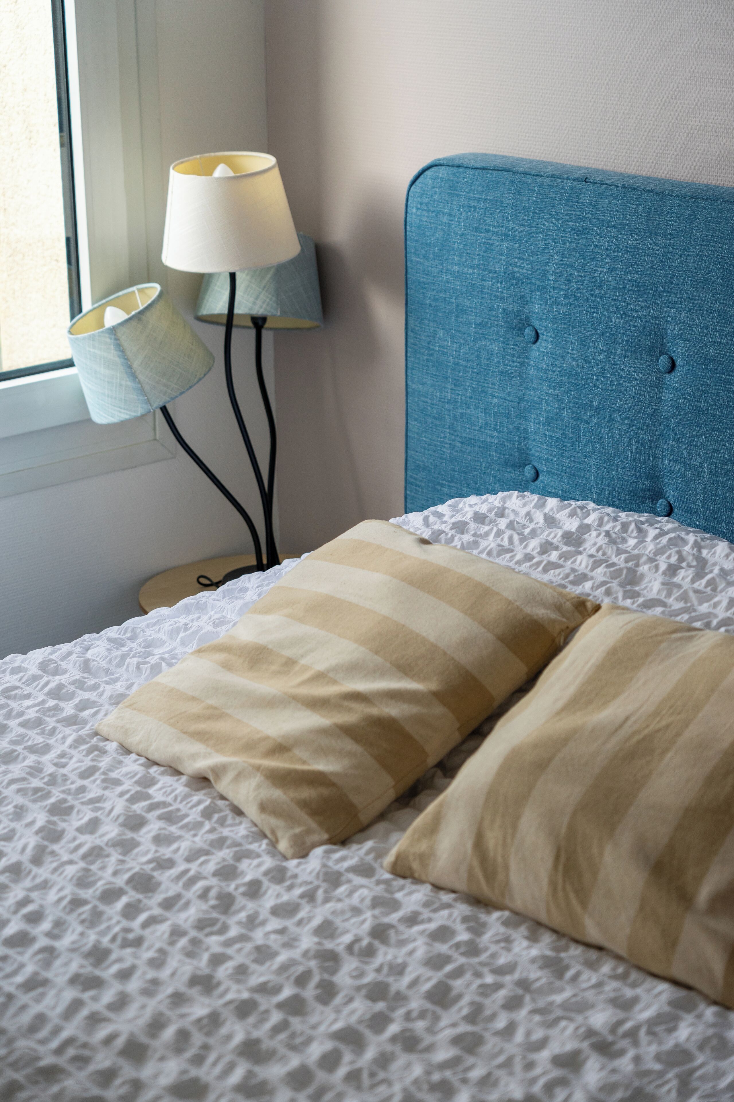 A neatly made bed with striped pillows, a blue headboard, and two bedside lamps.