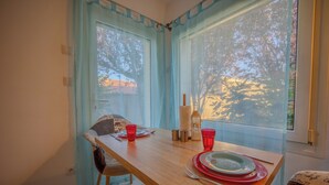 Una mesa de comedor servida con platos, cubiertos y vasos rojos, ubicada cerca de una ventana con cortinas azules.