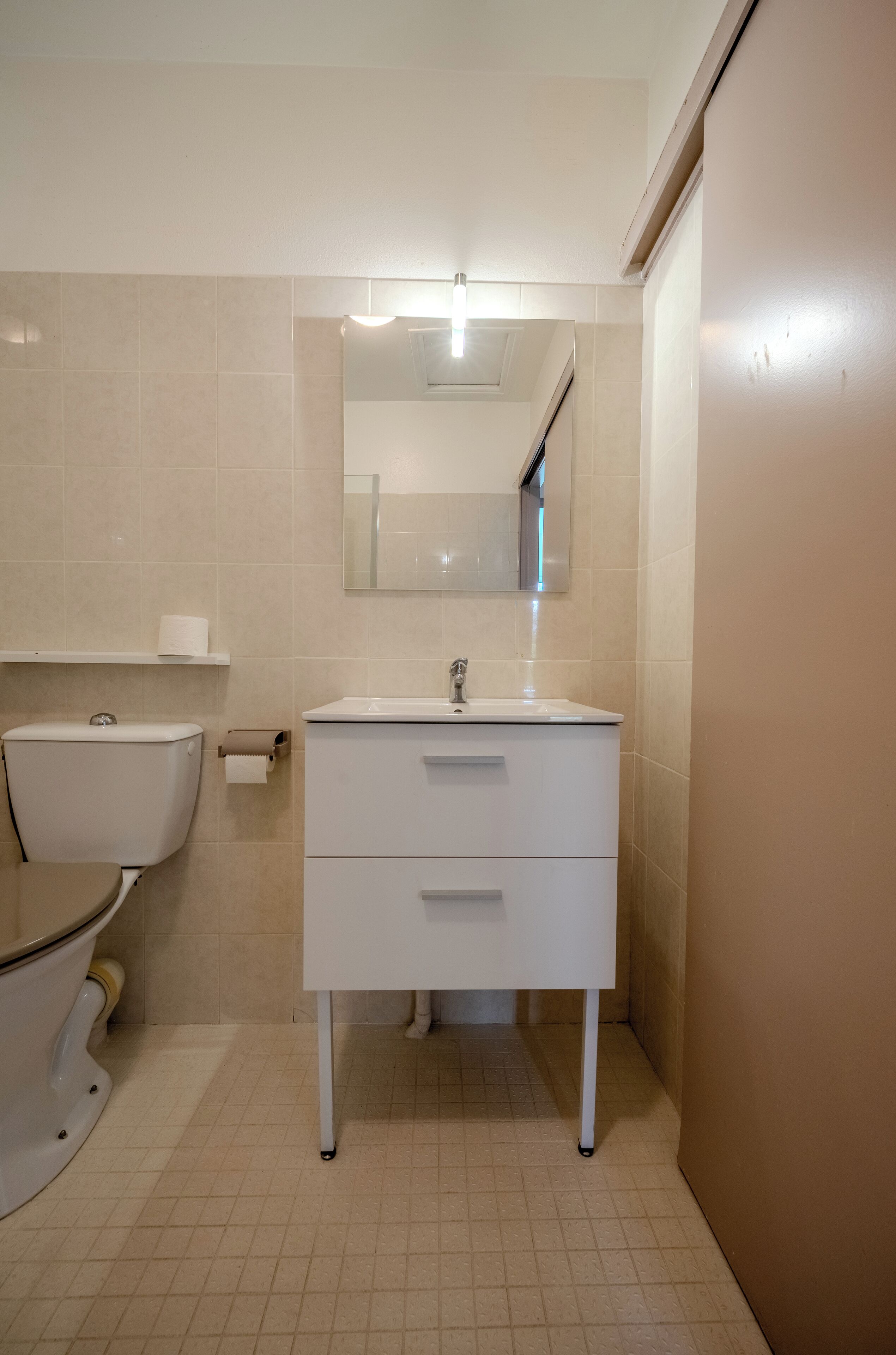 Un baño con inodoro, lavamanos, espejo y dispensador de toallas.