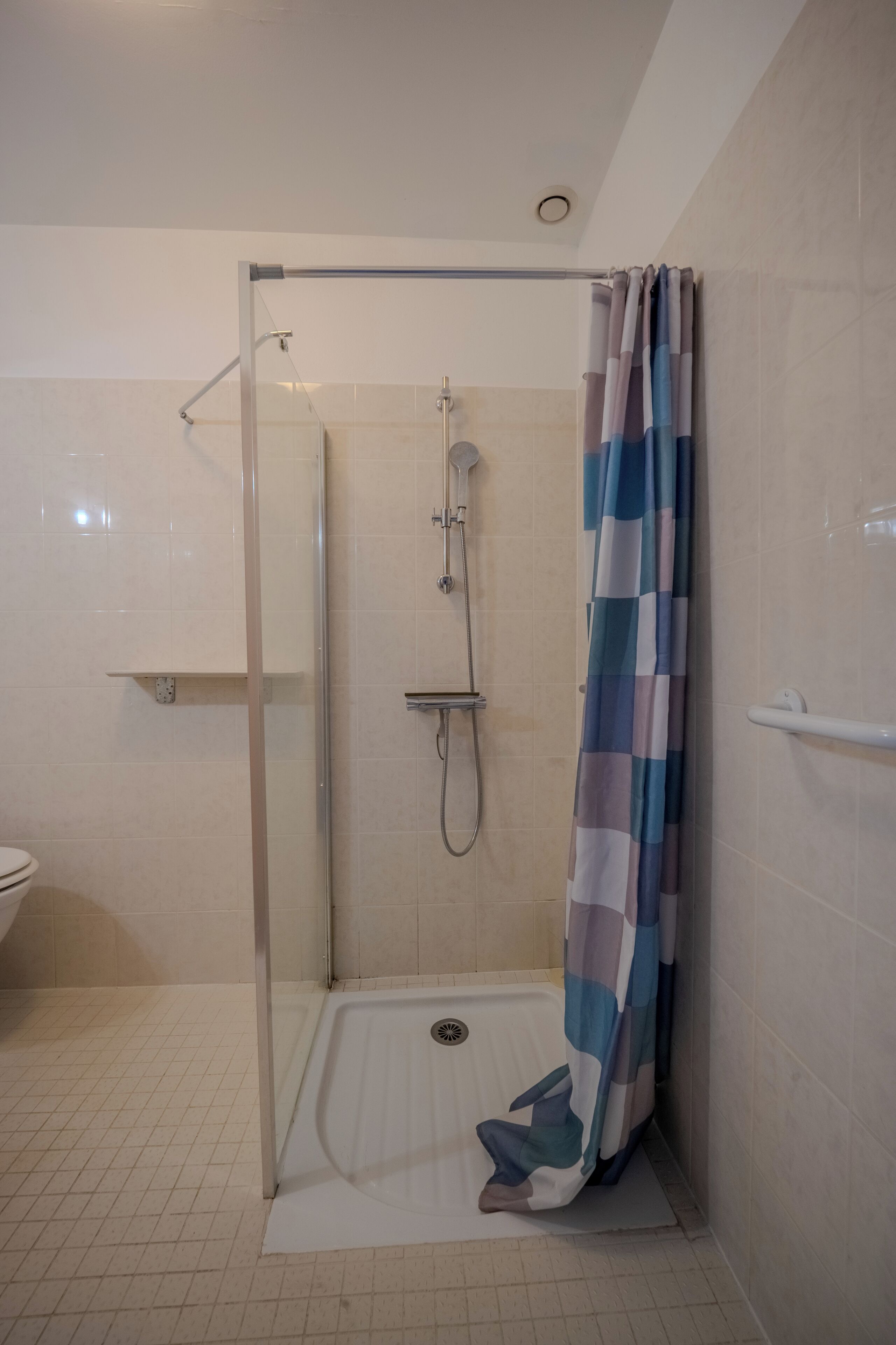Ducha con cerramiento de vidrio, cabezal de ducha, cortina y un lavamanos blanco a la izquierda.