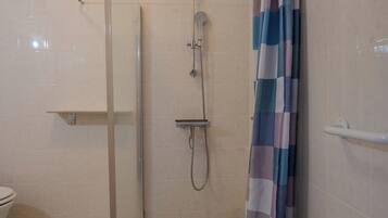 Ducha con cerramiento de vidrio, cabezal de ducha, cortina y un lavamanos blanco a la izquierda.