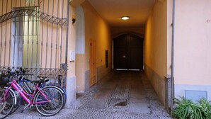 Ein schmaler Gang mit einem Fahrrad, das an einer Mauer lehnt, der zu einer verschlossenen Tür am Ende führt.