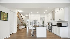 A modern kitchen with white cabinetry, a central island, and a wooden staircase leading to another room.