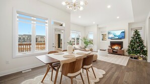 Un salón amplio con comedor, ventanas grandes, chimenea y un árbol de Navidad.