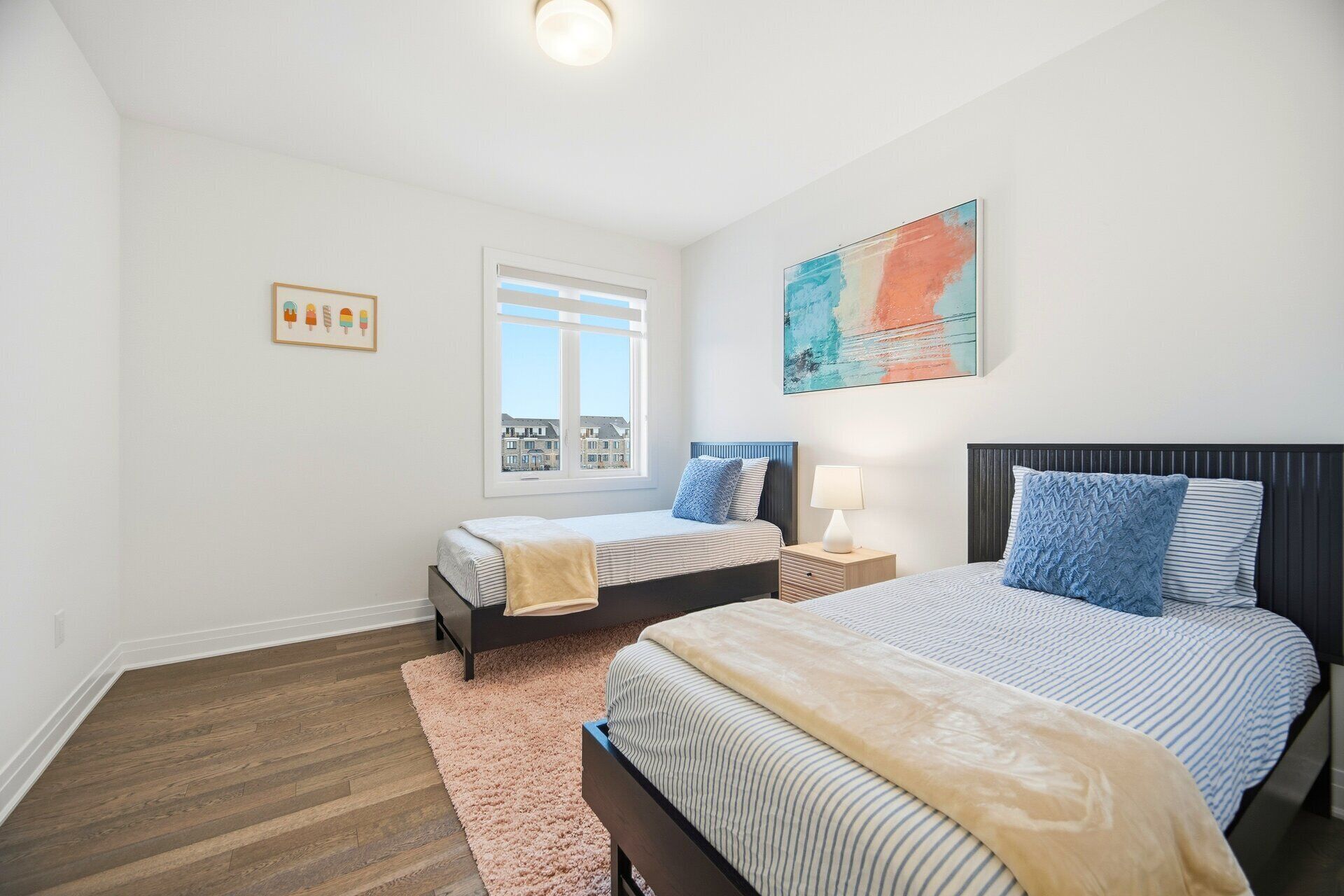 A bedroom with two beds, a large window, a city view, and a painting on the wall.