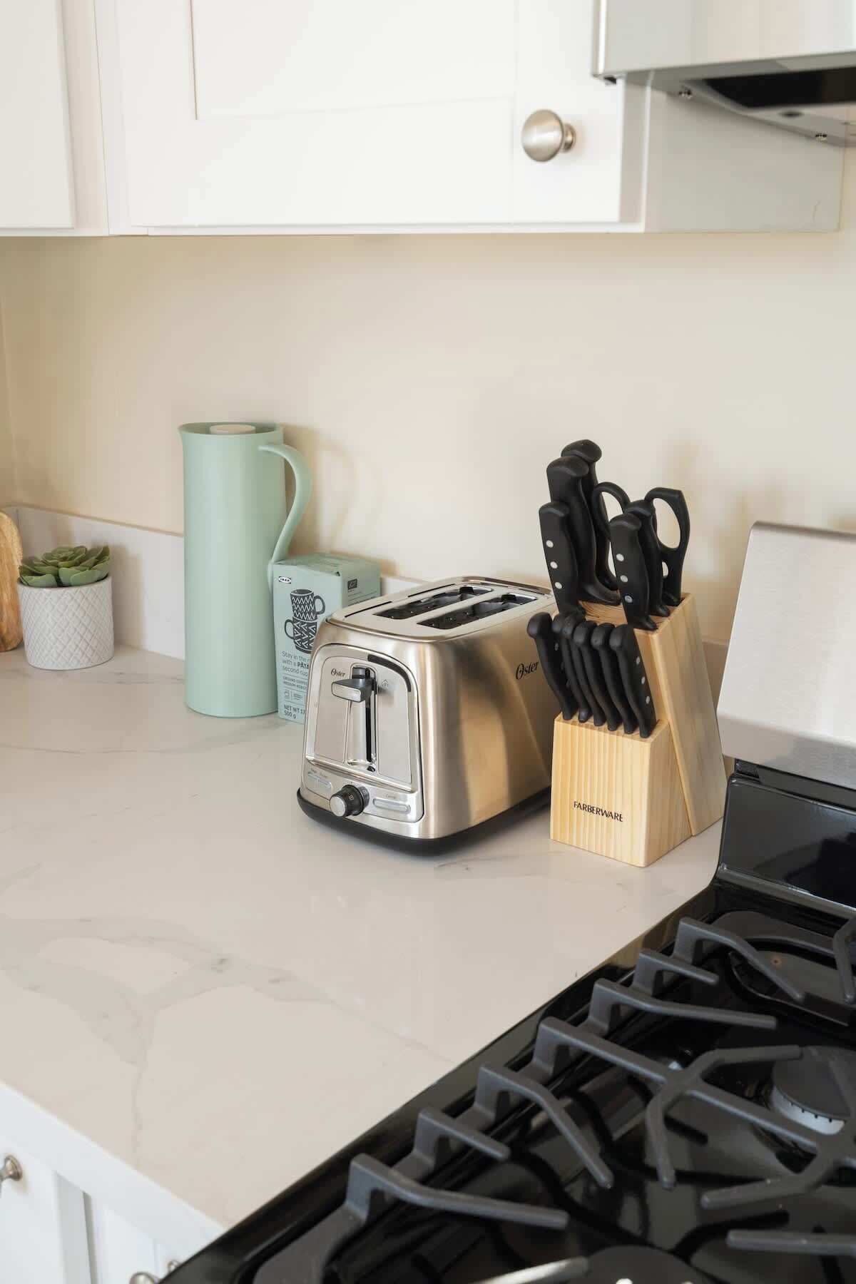 A kitchen with a stainless steel toaster, a knife block, a green mug, and a small potted plant on the counter.