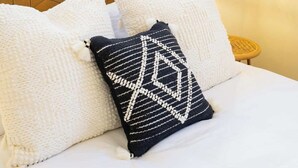 Un letto rifatto con cuscini a motivi bianchi e neri, una testiera a fantasia geometrica e un comodino con una lampada.