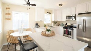 Una cucina moderna con mobili bianchi, un frigorifero in acciaio inossidabile, un forno a microonde e un piano cottura. C'è un'area pranzo con un tavolo rotondo e sedie.