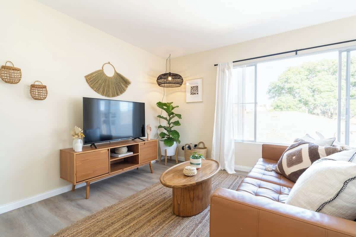 Un soggiorno moderno con una TV a schermo piatto, mobili in legno, un'ampia finestra con tende e decorazioni a parete.
