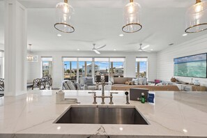 A spacious kitchen with a marble countertop, modern pendant lights, and a large window overlooking a scenic view. - Beach House - Seize the Bay  (Mexico Beach)