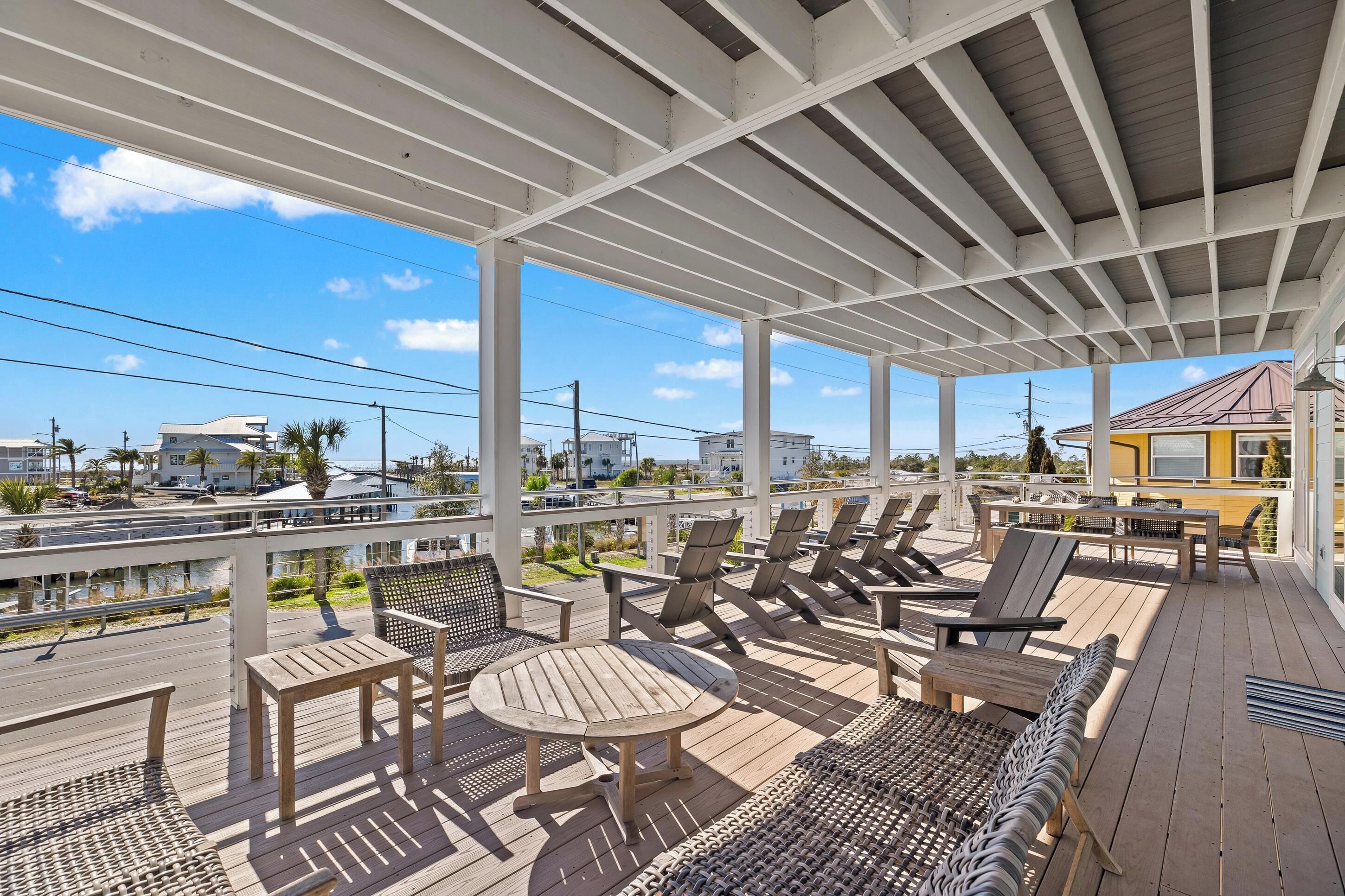 A covered outdoor deck with seating and tables, overlooking a road and buildings.