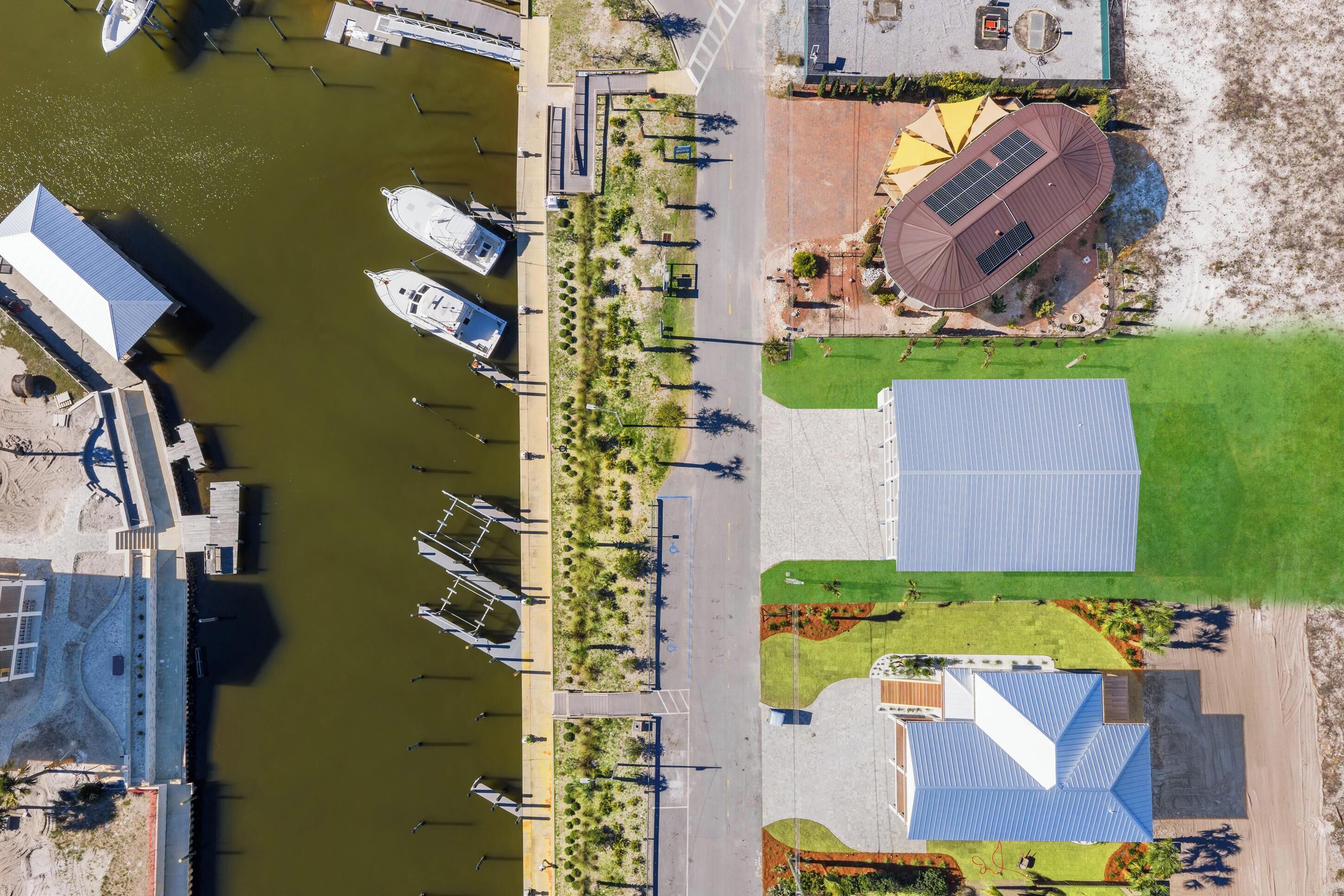An aerial view of a marina with boats docked, a pedestrian walkway, and a building with a solar panel roof.