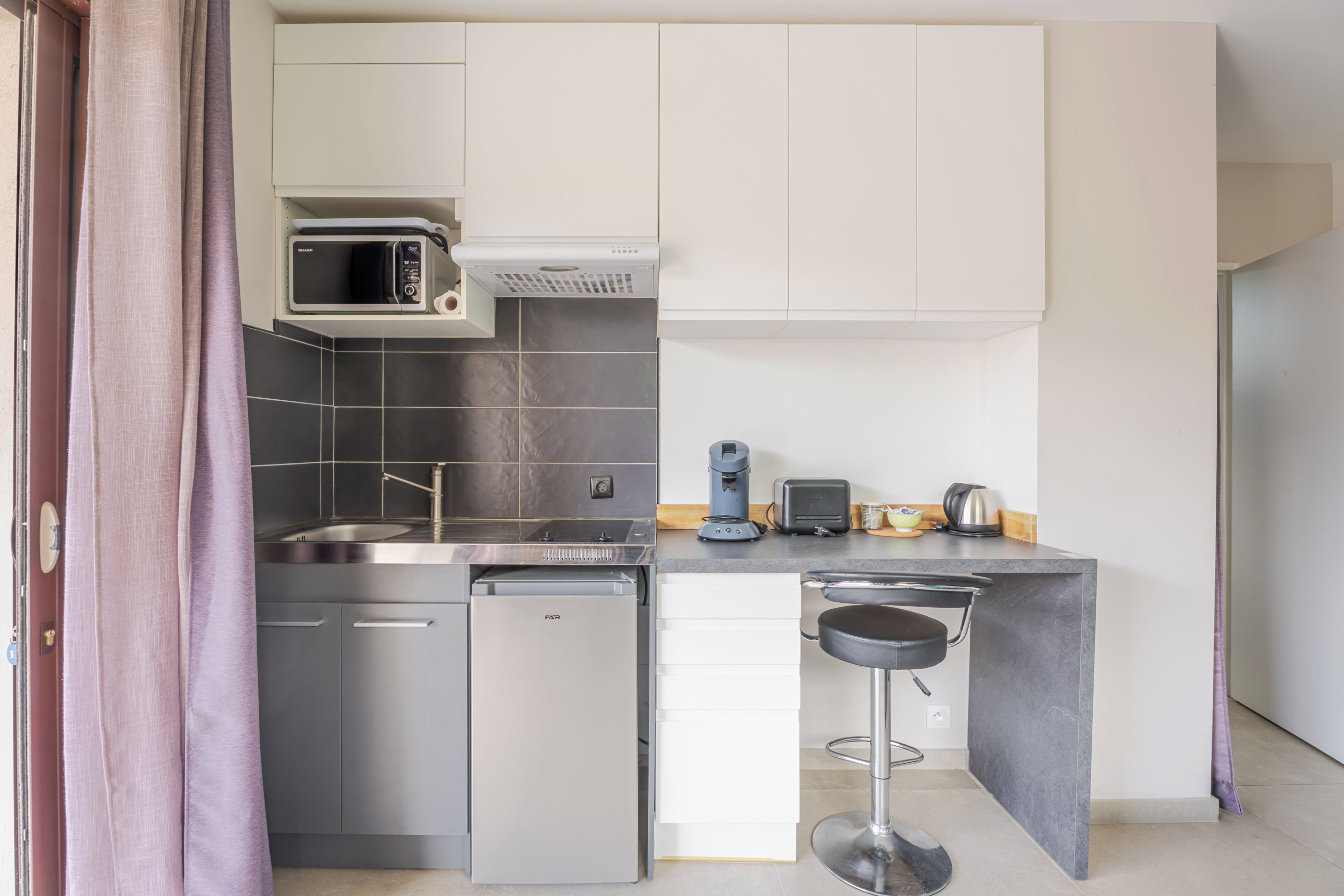 Een kleine keuken met een magnetron, koffiezetapparaat en een koelkastje.